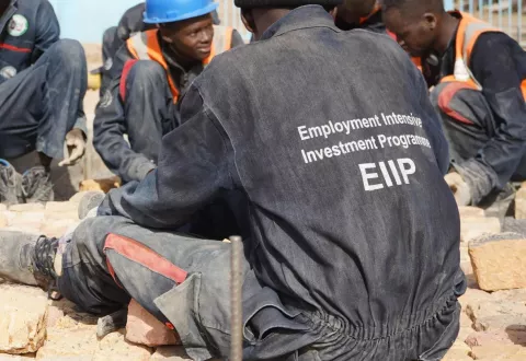Image of youth resting in a group on a building site wearing a jacket with labels of EIIP on the back