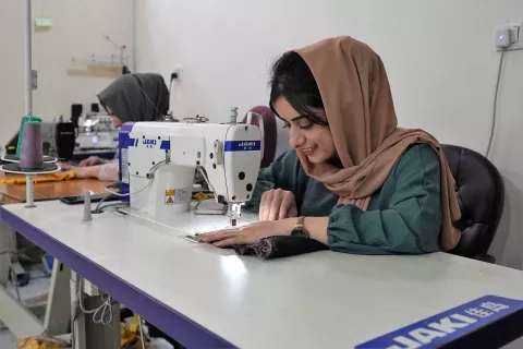 Image of two ladies wearing headscarves sewing clothes on sewing machines