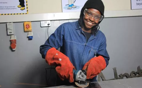 Image of a female trainee working on cutting metals with protect gloves and protect glasses on